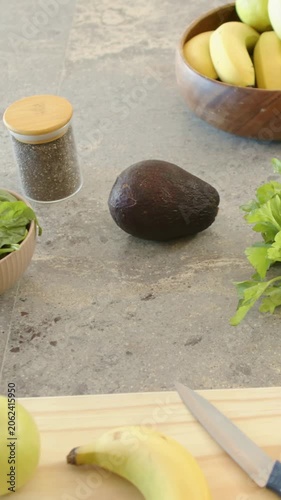 Vertical video: Recording cam capturing center avocado sitting on counter with knife, board to prep