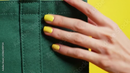Woman with yellow manicure touching green canvas bag against yellow background