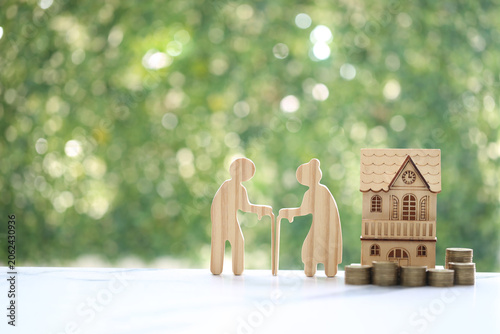 Couple wooden figures standing with a miniature house and coins, representing retirement home planning, property investment, real estate for seniors and financial security for old age.