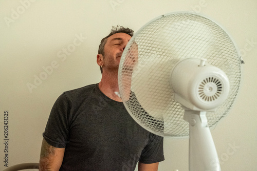 Fotografie A man enjoys the coolness of the fan up close to counteract the summer heat