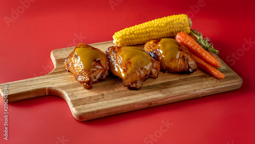 Glazed Chicken Thighs with Crispy Grill Marks and Roasted Vegetables on Wooden Board Red Background BBQ Scene