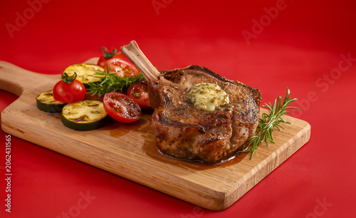 Lamb Shoulder Chop with Garlic Herb Butter, Roasted Vegetables and Rosemary on Red Background BBQ Braai Scene