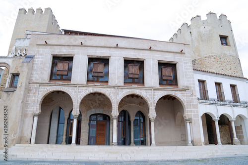The historic Old Town Hall buildings featuring mudejar style arches and wooden lattices with the medieval fortress towers of the Alcazaba in the background in Badajoz, Extremadura, Spain.