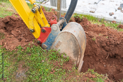 Mini excavator bucket digging a garden trench. Compact digger machine excavating soil on lawn