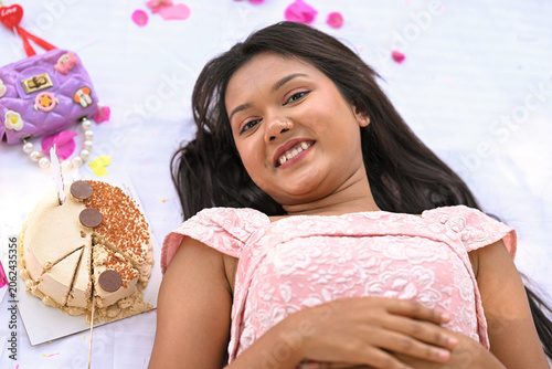 Relaxed attractive delighted India woman resting in park smiling and enjoying the springtime wearing casual attire and lying on plaid blanket during birthday party and cake.