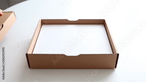 Hands opening a brown cardboard box on a white table to reveal contents