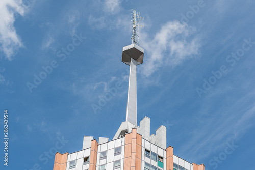 Low angle view of a telecommunication tower and antennas on top of a high-rise building against blue sky. Radio mast and cellular transmitter station on a residential skyscraper roof. Wireless network
