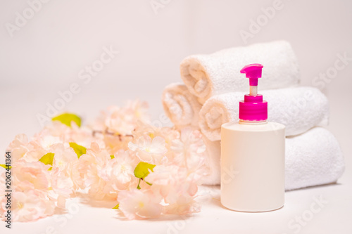 Fotografie Minimalist spa still life with a blank white cosmetic pump bottle mockup, rolled cotton towels and soft pink cherry blossoms on a clean background