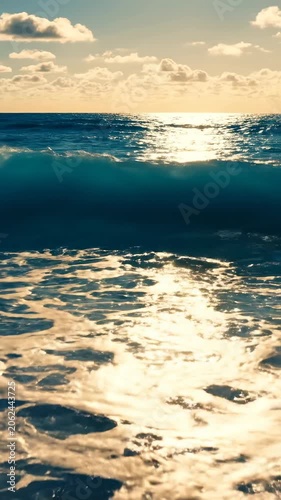 Golden sun reflecting on a powerful ocean wave crashing near shore, bright sky with soft clouds, dynamic seascape