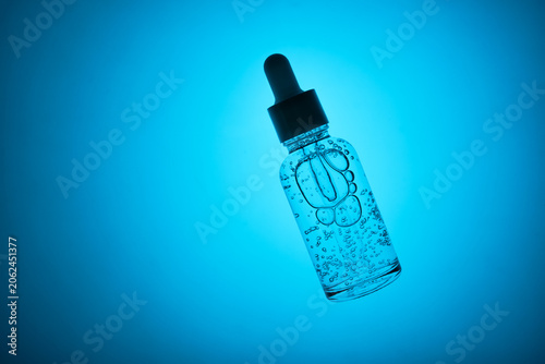 Dropper bottle filled with serum, displaying bubbles and pipette on blue background