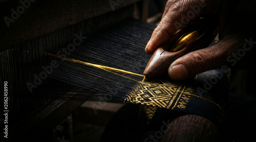 Close up of artisan hands weaving intricate traditional Thai golden silk textile on a wooden loom