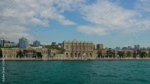Magnificent Dolmabahce Palace architecture located on the waterfront of Istanbul with turquoise sea in the foreground and a modern city skyline under a bright blue sky