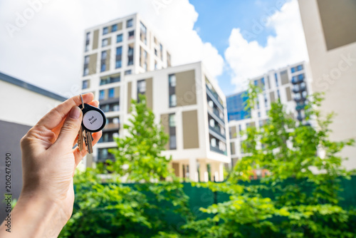 Foto Hand holding house keys with Real Estate keychain near modern apartment building