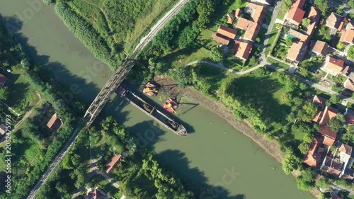Above top view, dolly move downward over two excavators dredge as dredging, work on river, canal, deepening and removing sediment, mud from riverbed in a polluted waterway near old railroad bridge.