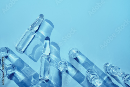 Ampoules containing clear liquid medicine casting strong shadows on blue surface