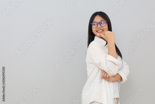 A beautiful and cheerful young Asian woman is seen from the side, smiling while pointing and glancing sideways at an empty space, displaying an advertisement, standing isolated on a white background.
