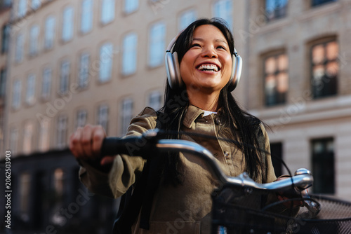 Smiling woman with bicycle and headphones in city