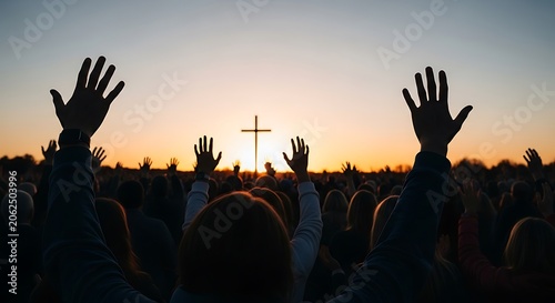 A crowd with raised arms faces a cross at sunset, a scene of worship and faith