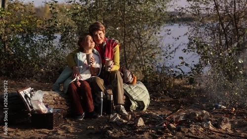 Little child girl with grandpa and grandmother Having a picnic on the beach on a sunny autumn day. Concept of friendly family.  Family  roasts marshmallows and sausages on the campfire.