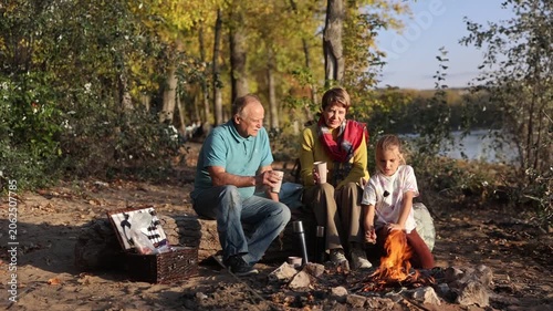 Little child girl with grandpa and grandmother Having a picnic on the beach on a sunny autumn day. Concept of friendly family.  Family  roasts marshmallows and sausages on the campfire.