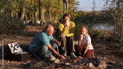 Little child girl with grandpa and grandmother Having a picnic on the beach on a sunny autumn day. Concept of friendly family.  Family  roasts marshmallows and sausages on the campfire.