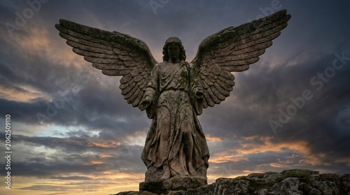 Stone statue of an angel with spread wings against a dramatic sunset sky.