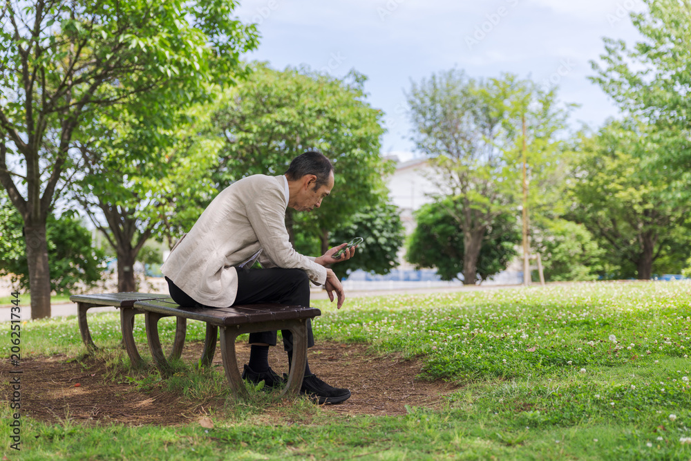 Fototapeta premium 公園のベンチでスマートフォンを見る日本人男性