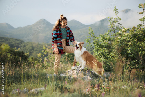 Woman spends time with Border Collie surrounded by mountain scenery and greenery. Outdoor setting creates calm adventure mood.