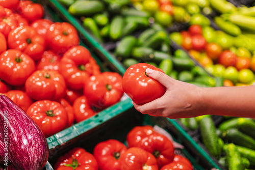 Woman selecting ripe tomato at supermarket fresh produce display