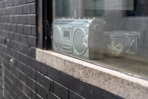 Vintage silver boombox sits on a windowsill behind glass