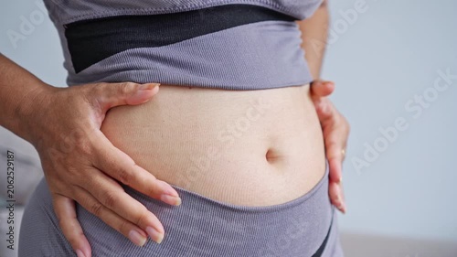 close-up of a woman in grey athletic wear pinching her belly fat, representing body weight struggles, fitness goals, healthy lifestyle changes, body positivity, and obesity concern