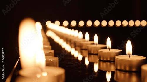 Burning tea light candles flickering on a dark reflective surface.