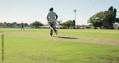Cricket bat and helmet are resting on trimmed green pitch, featuring light pole, houses