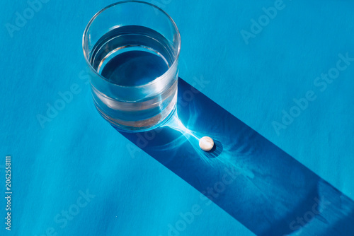 Foto One medicine tablet pill in a sun caustic light flare near a glass of clean water