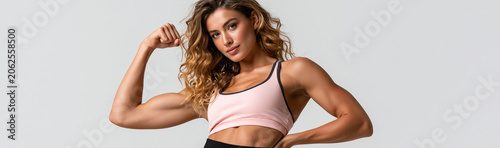 Fitness Icon: A strong, athletic woman proudly flexes her bicep, showcasing sculpted muscles and radiating confidence in her fitness journey.