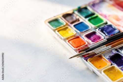 Watercolor paint palette with vibrant colorful pans and professional brushes resting on white textured surface in bright studio light, creative art concept with copy space