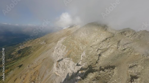 Dynamic FPV drone pass tracing a narrow alpine ridgeline while mist drifts across the crest, exposing raw rock faces, steep dropoffs, and expansive mountain scenery in cinematic motion