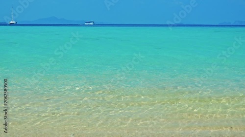Shallow turquoise sea water rippling, tropical ocean environment with distant boats on horizon, summer travel and vacation background