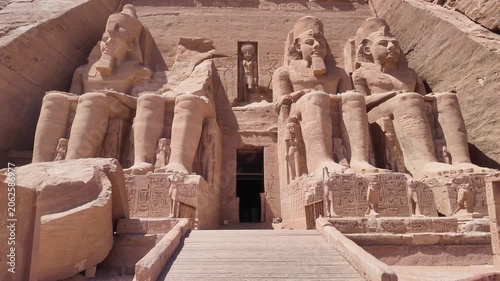 First person view walking through the Majestic facade of the great temple of Abu Simbel in Egypt. Four colossal seated statues of pharaoh ramses ii guarding the entrance
