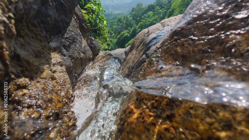 Close up of clear water flowing between granite rocks at Na Muang Waterfall 2 on Koh Samui, Thailand. Dynamic tropical waterfall scene with rainforest valley