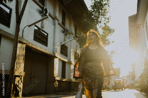 Schilderij op canvas Confident adult Asian woman in batik clothes walking in golden hour sunlight on the halfway city street