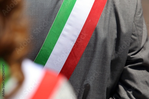 Close-up of an Italian mayor wearing the official tricolor sash over a grey suit during a public ceremony