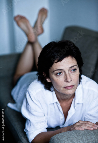 Melancholie und Ruhe: Elegante Frau mittleren Alters entspannt nachdenklich auf einer Couch.
