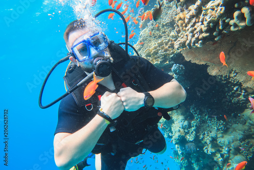 Tableau sur toile Male scuba diver underwater looking at camera next to vibrant coral reef with sc