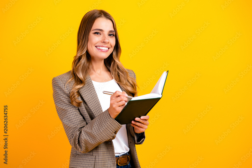 Fototapeta premium Smiling businesswoman writing in notebook against a bright yellow background, planning, taking notes and staying organized for work and personal projects