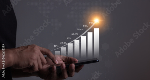 Young man using smartphone to visualize money growth The phone screen displays graphs and charts showing increasing investment and savings trends, along with an increased account balance