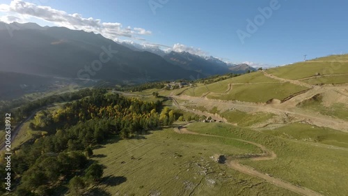Cinematic fpv drone flight over alpine meadow and forest, passing a mountain hut and continuing above dirt road with a pickup truck driving through scenic highland landscape 