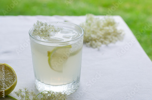 Foto Glass with elderberry drink and lemon slices, ice and elderflowers on a light background