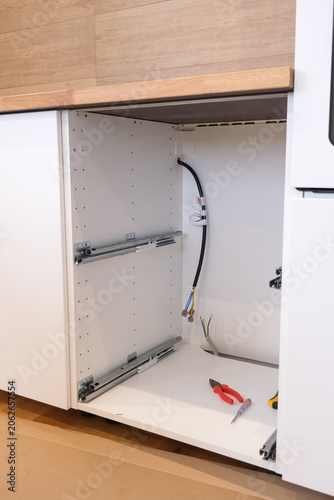 Open white kitchen cabinet with mounting hardware and tools