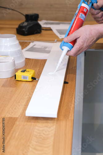Hands apply white sealant to wooden plank on workbench